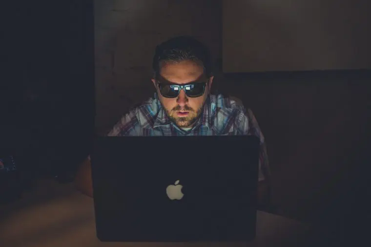 Photograph of man with sunglasses using a computer in the dark